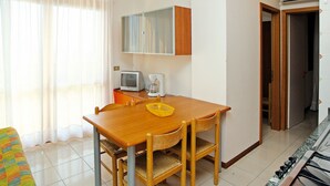 Una cocina compacta con una mesa de madera, sillas, un televisor pequeño y una cafetera.