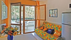 Una habitación con sofá, una mesa con un jarrón de flores, televisión y refrigerador.