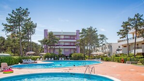 A swimming pool area with two pools, lounge chairs, and a building in the background.