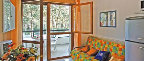 A room with a sofa, a table with a vase of flowers, a television, and a refrigerator.