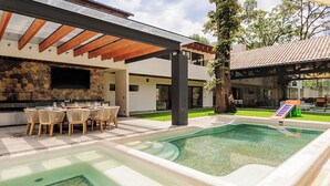 A modern outdoor pool area with a stone wall, a dining setup, and a covered patio. - Casa Ripoll (Valle de Bravo)