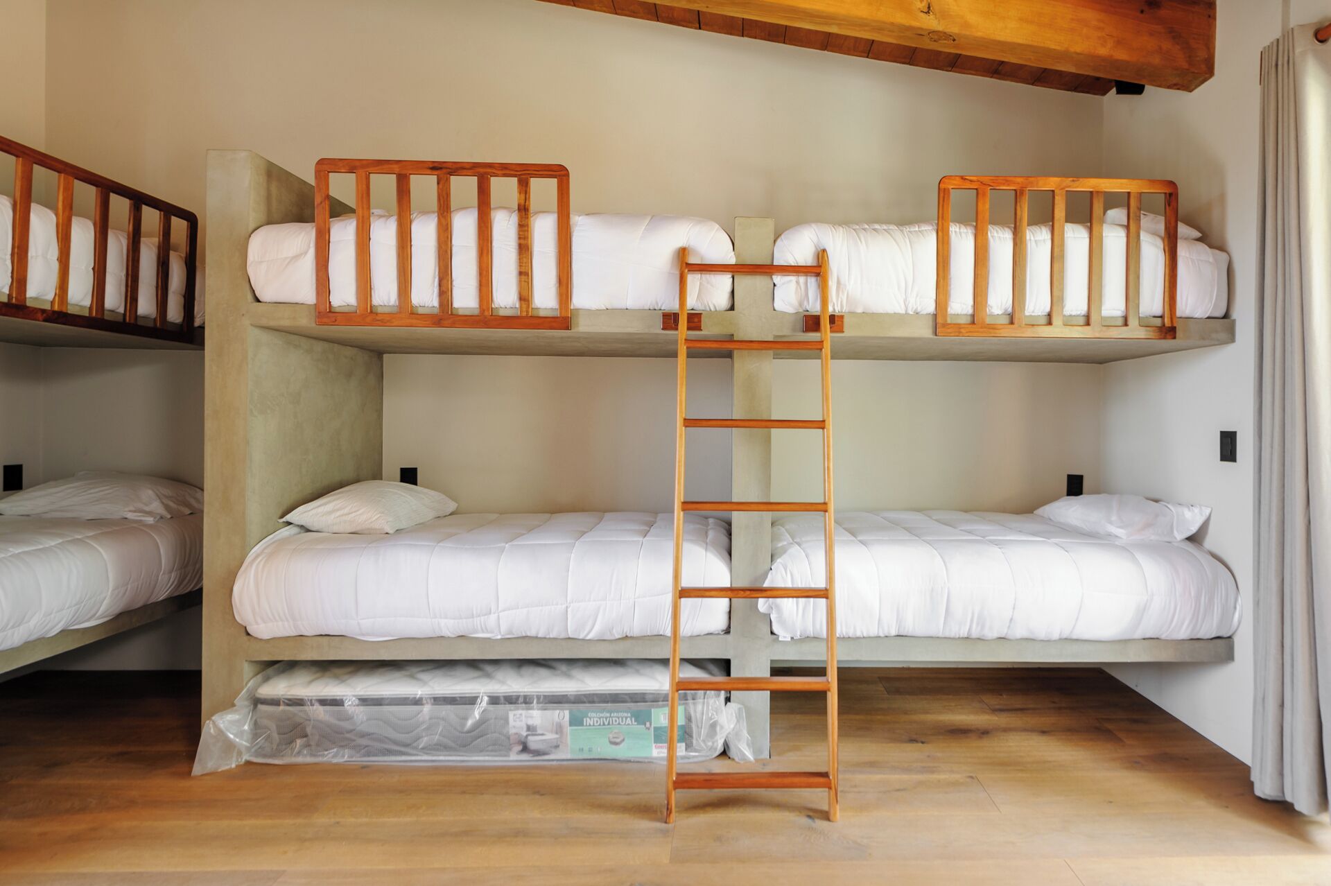 A bunk bed room with a wooden ladder, white bedding, and a wooden floor.