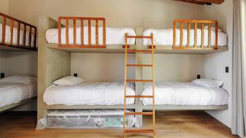 A bunk bed room with a wooden ladder, white bedding, and a wooden floor.