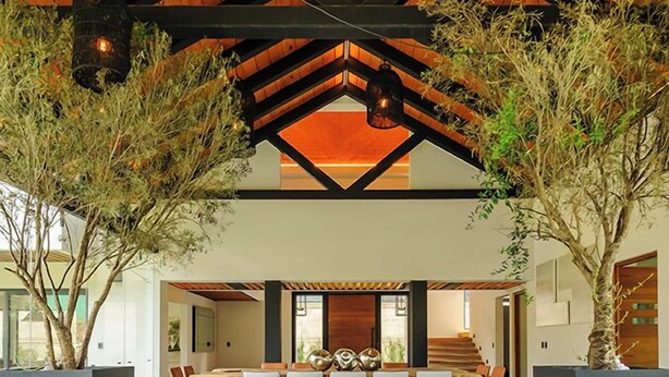 A modern living room with a large sectional sofa, wooden ceiling beams, and potted plants. - Casa Ripoll (Valle de Bravo)