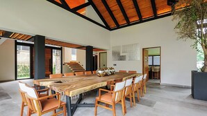 A spacious dining area with a long wooden table surrounded by chairs, a staircase in the background, and a large potted plant. - Casa Ripoll (Valle de Bravo)
