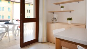 A modern kitchen with a coffee maker, two potted plants, and a flat-screen TV on a wall shelf. - Torcello by Interhome (Bibione)