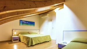 Une chambre avec un plafond en bois, un lit recouvert d’une couverture verte, une table de chevet avec une lampe et une petite table sur laquelle se trouve un livre.