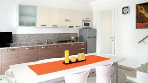 Une cuisine moderne dotée de plans de travail en granit, d’un réfrigérateur en acier inoxydable et d’un four à micro-ondes. On y trouve une table à manger avec des chaises blanches et un set de table rouge.