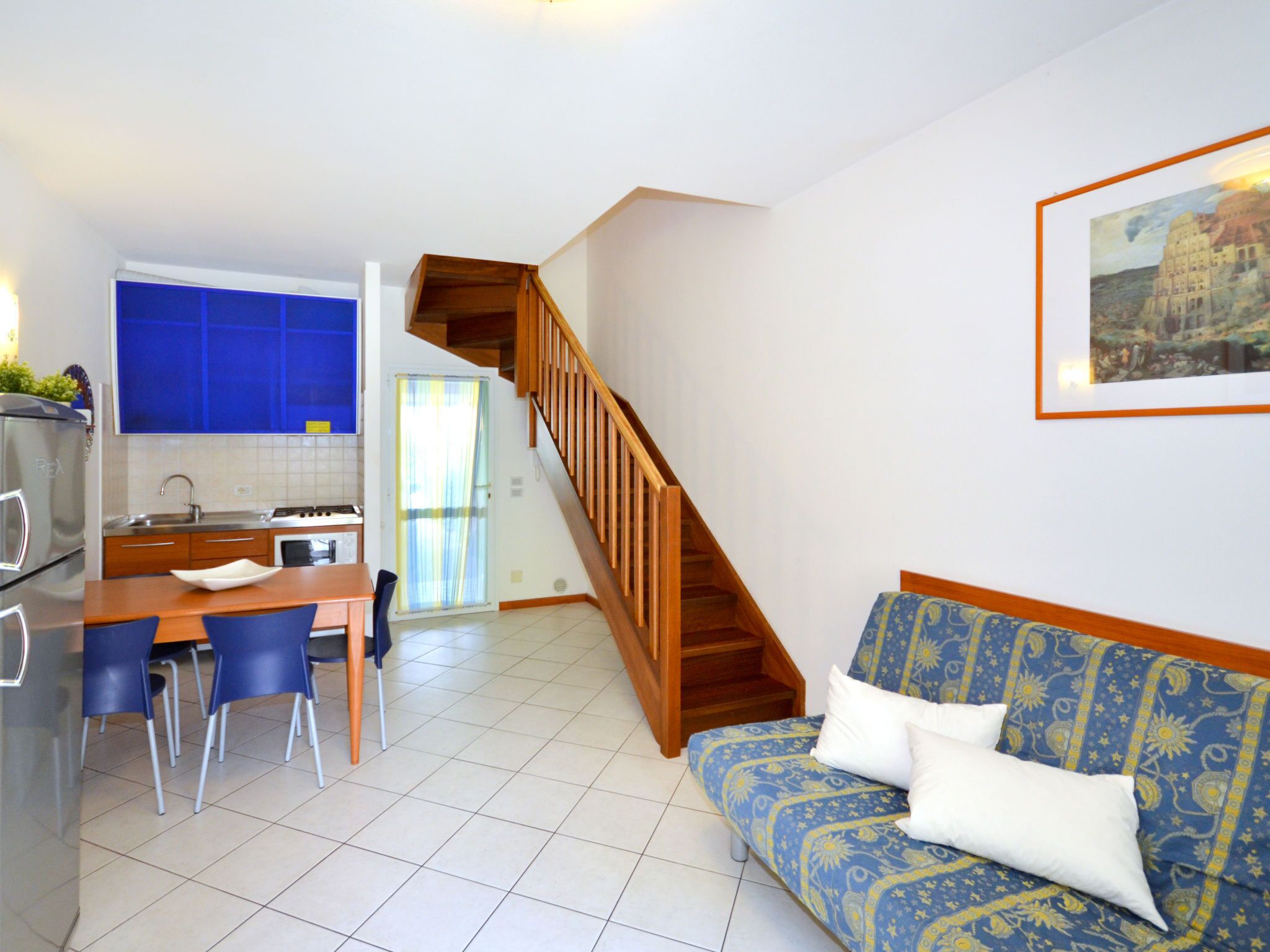 Un espacio habitable compacto con cocina, comedor y una escalera que sube a otro nivel.