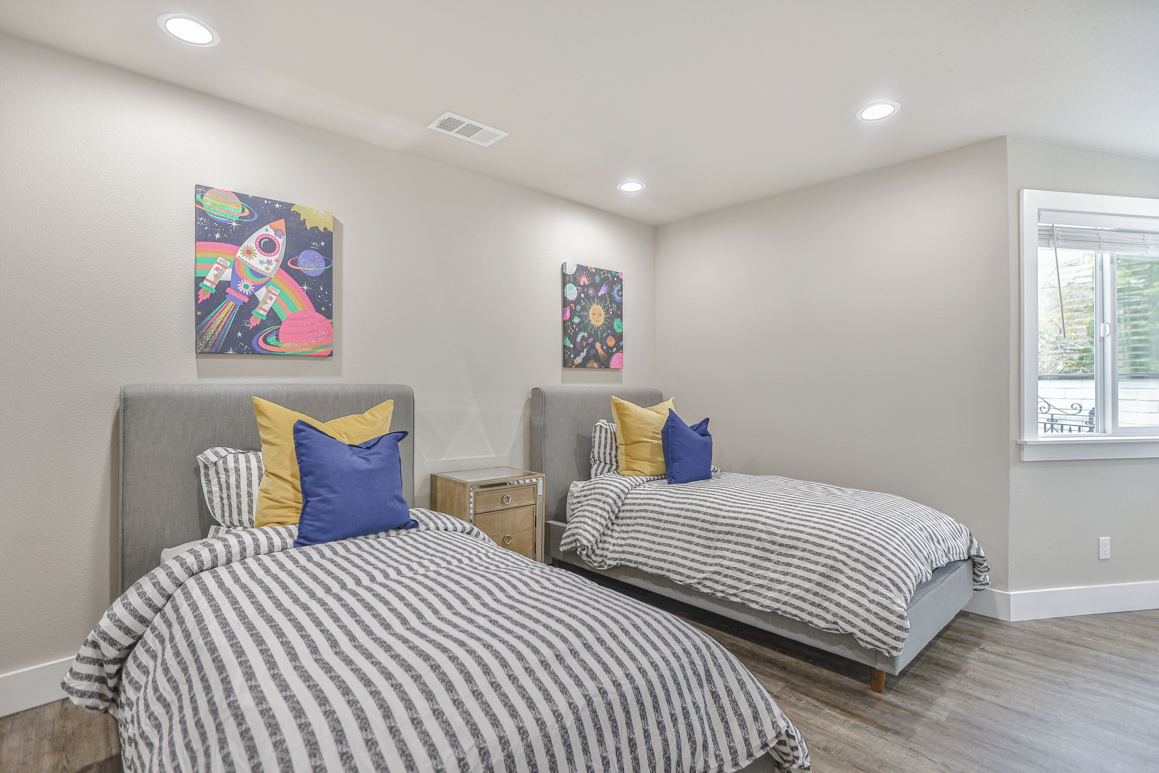 A bedroom with two beds, each with striped bedding and pillows, a nightstand, and two wall-mounted paintings.