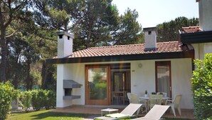 A modern house with a tiled roof, a patio with two lounge chairs, and a glass door leading to an interior space.