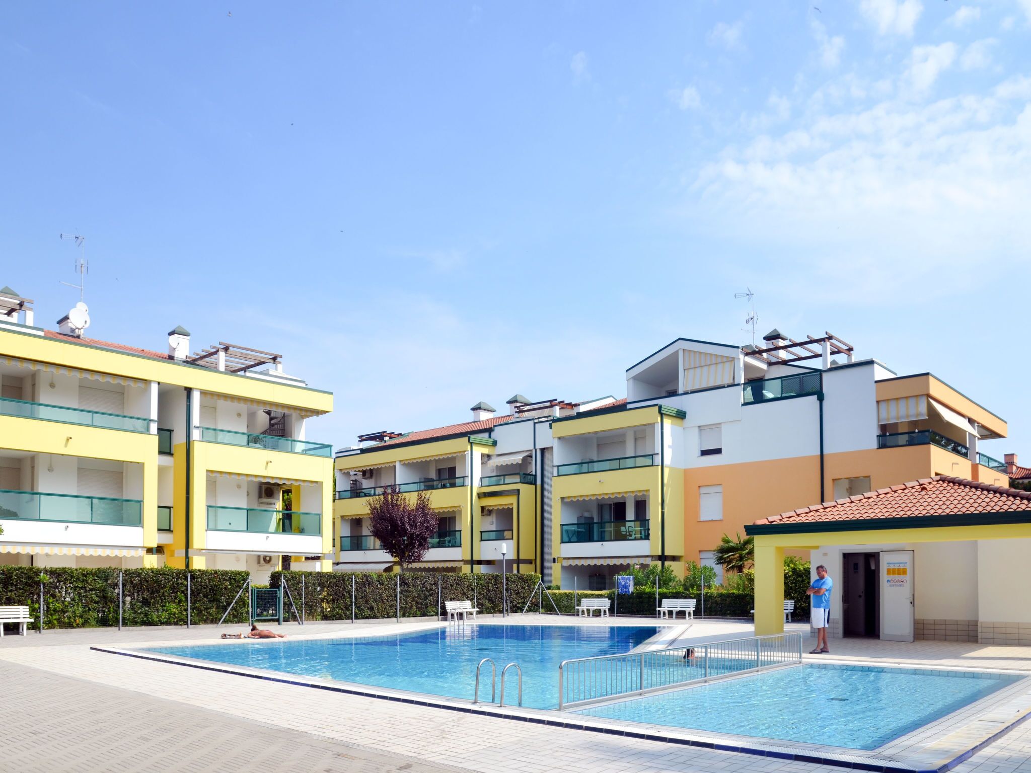 A modern hotel with a swimming pool, multiple balconies, and a clear sky.