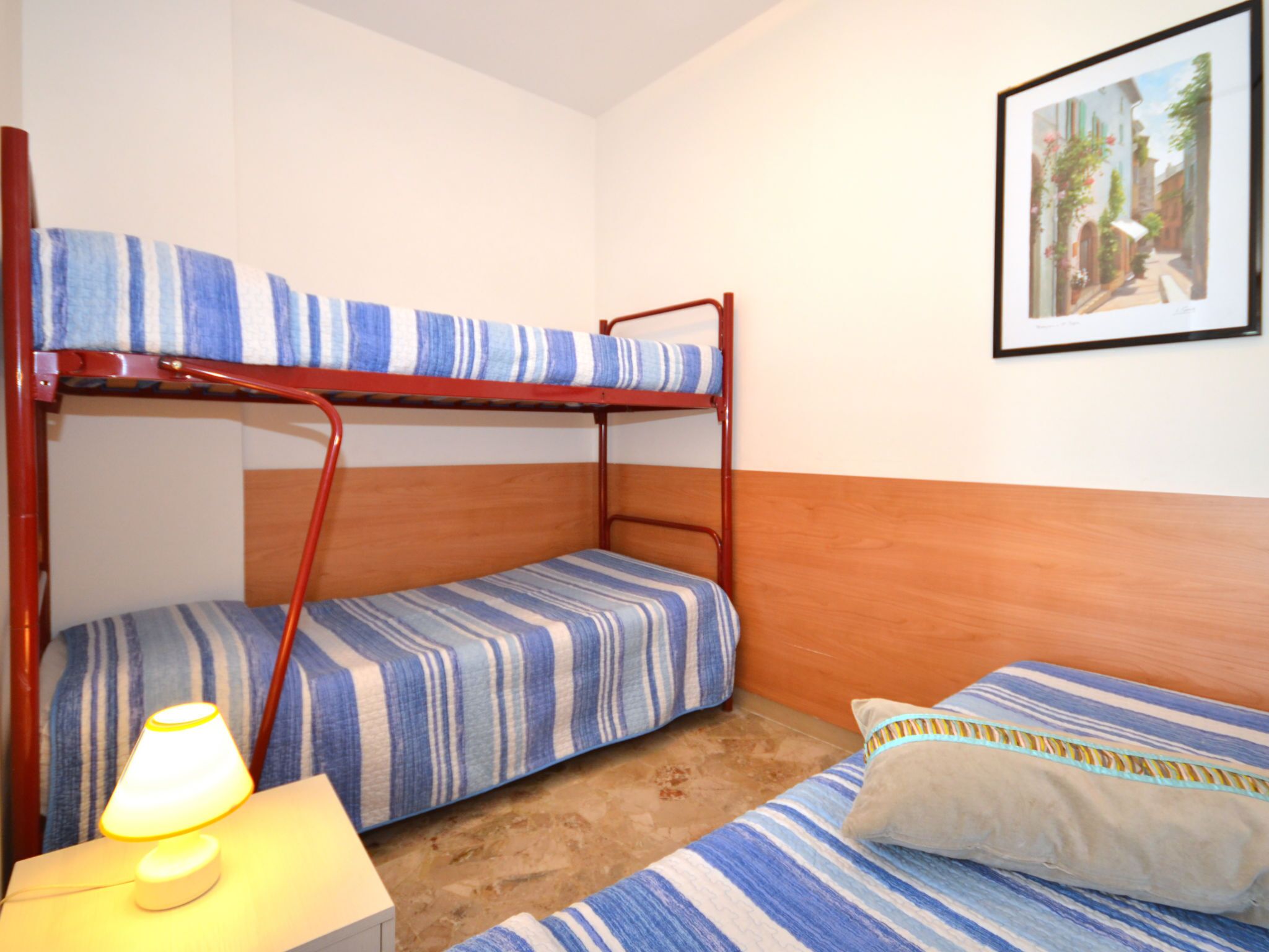 Ein Schlafzimmer mit Etagenbetten, gestreifter Bettwäsche, einer Nachttischlampe und einem gerahmten Bild an der Wand.