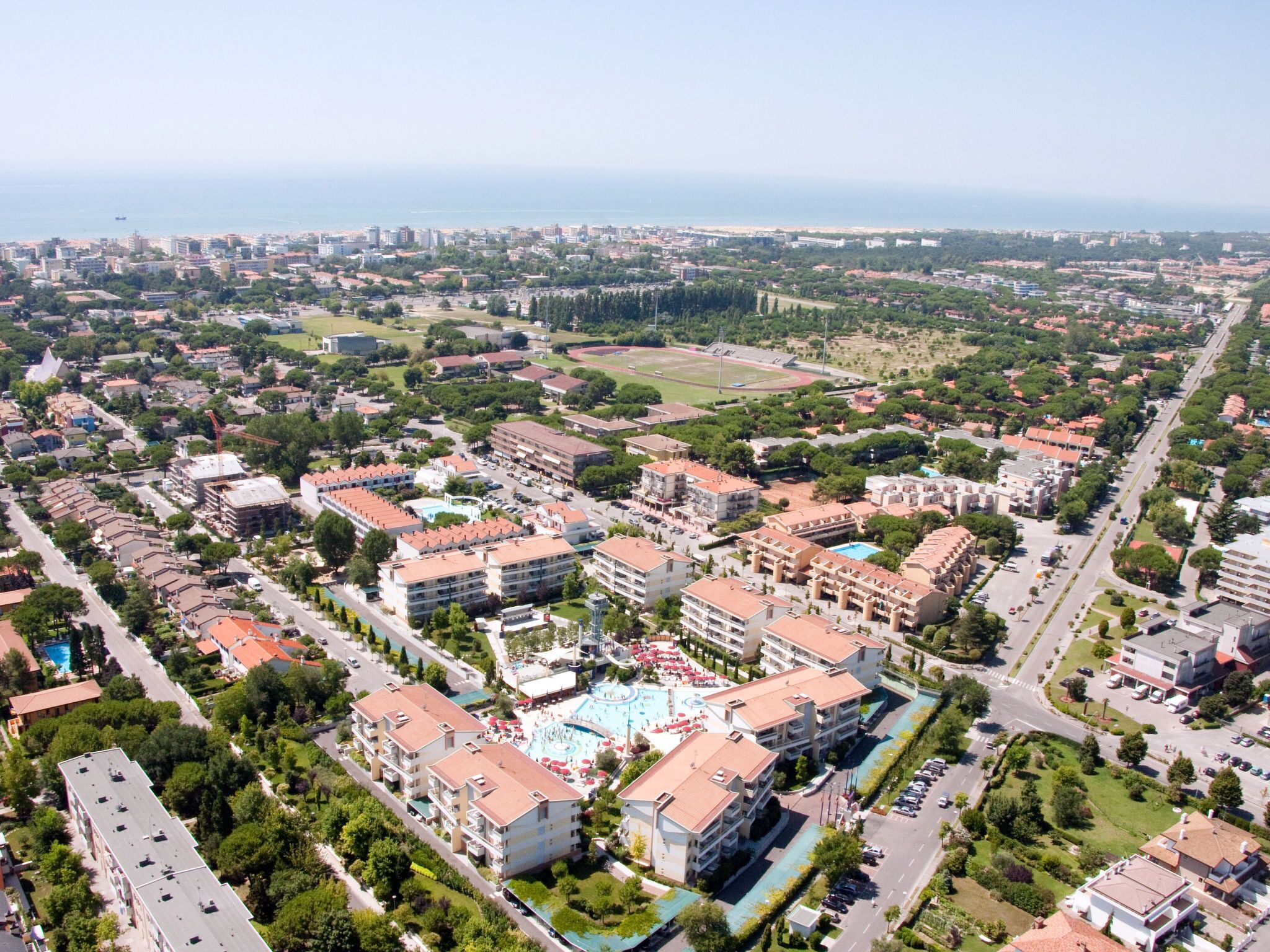 Vista aérea de un área residencial con varios edificios de apartamentos, una piscina central y un campo deportivo.
