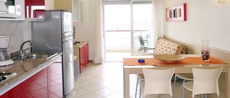 A compact kitchen with a refrigerator, microwave, and sink. There is a dining area with a table and chairs, and a balcony with a view.
