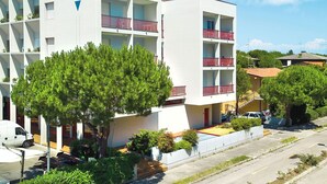 Un edificio moderno de varios pisos con balcones, zona de estacionamiento y áreas verdes circundantes.