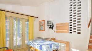 Una stanza con un tavolo da pranzo, sedie, una panca, una TV e una finestra con tende.