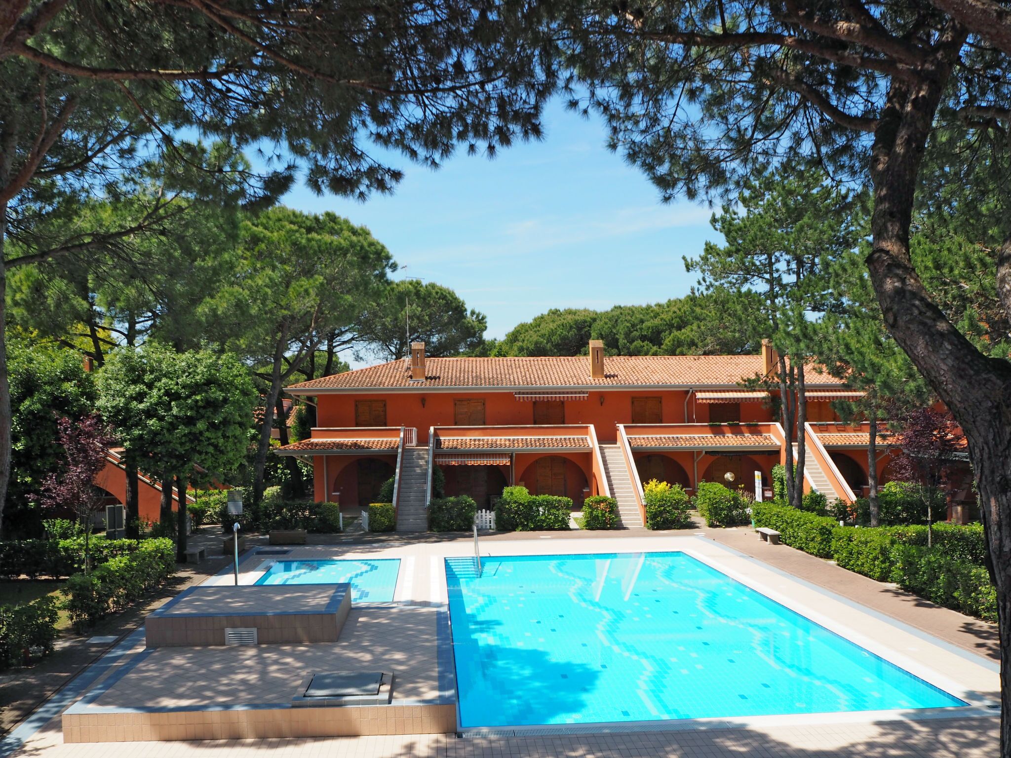 A resort with a swimming pool, a covered patio, and a building with a tiled roof.