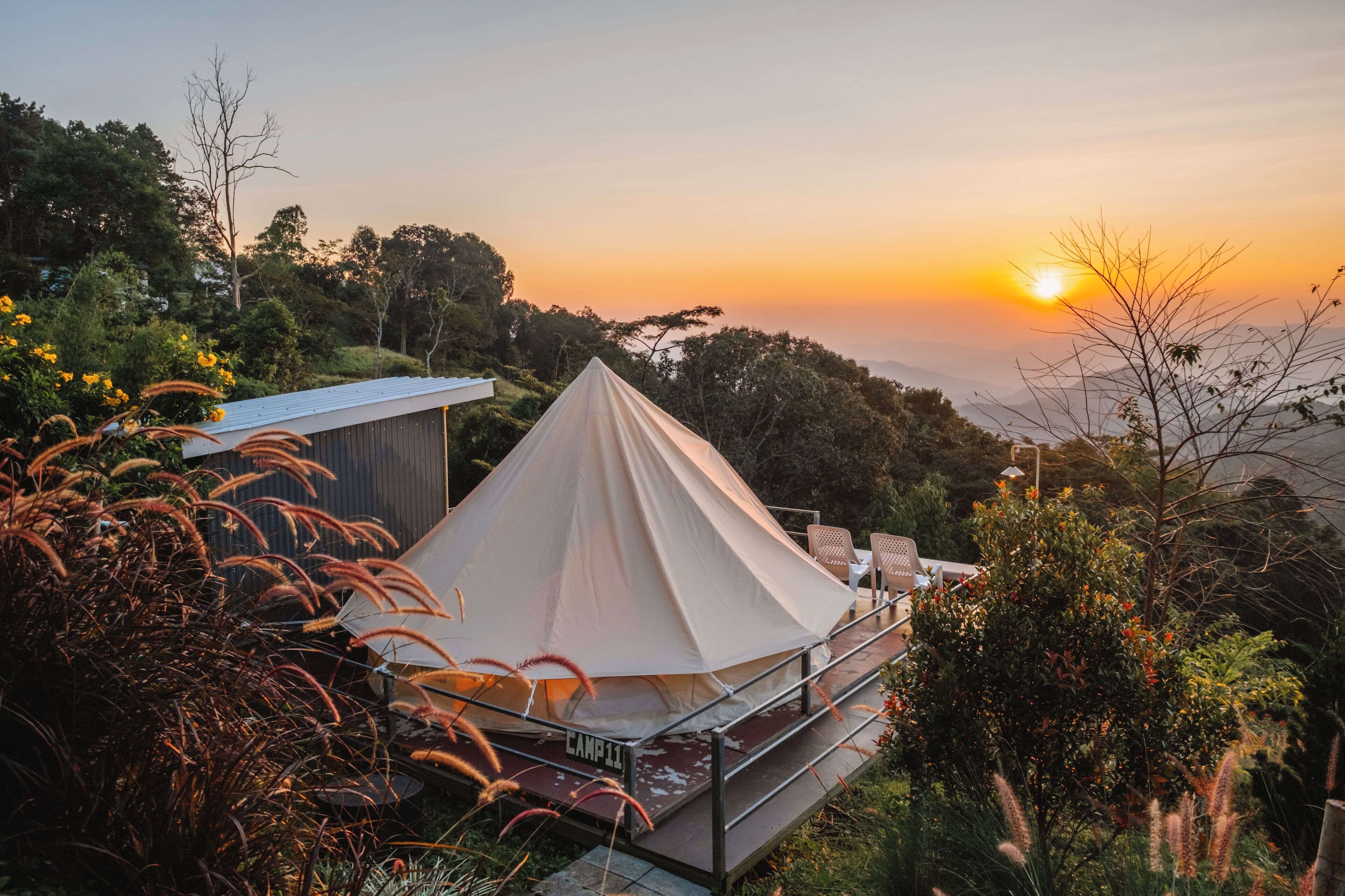 Une tente conique dotée d’une plateforme et de garde-corps, entourée d’une végétation luxuriante et offrant une vue imprenable sur le coucher du soleil.