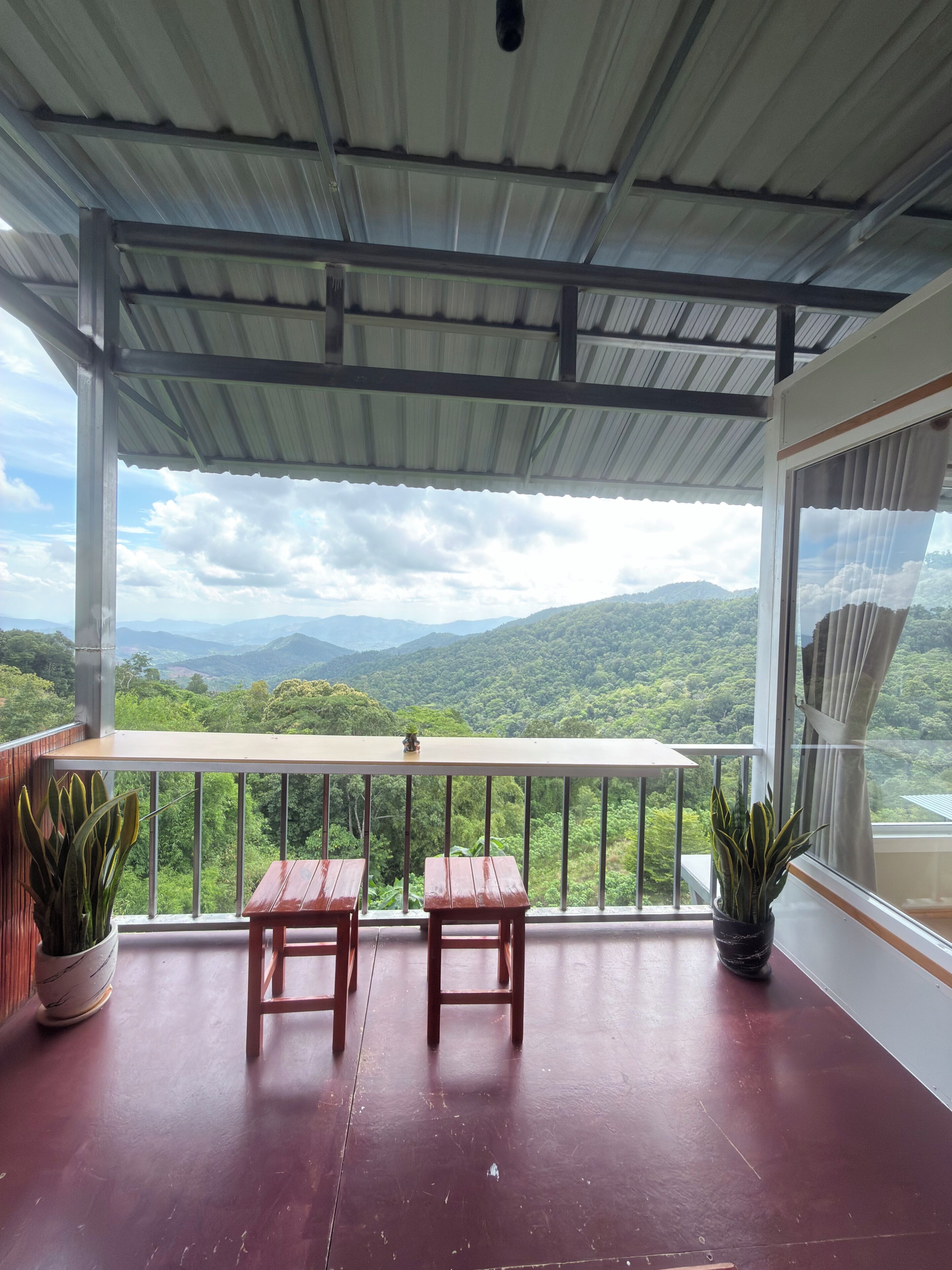 A balcony with two wooden tables, potted plants, and a view of green hills.