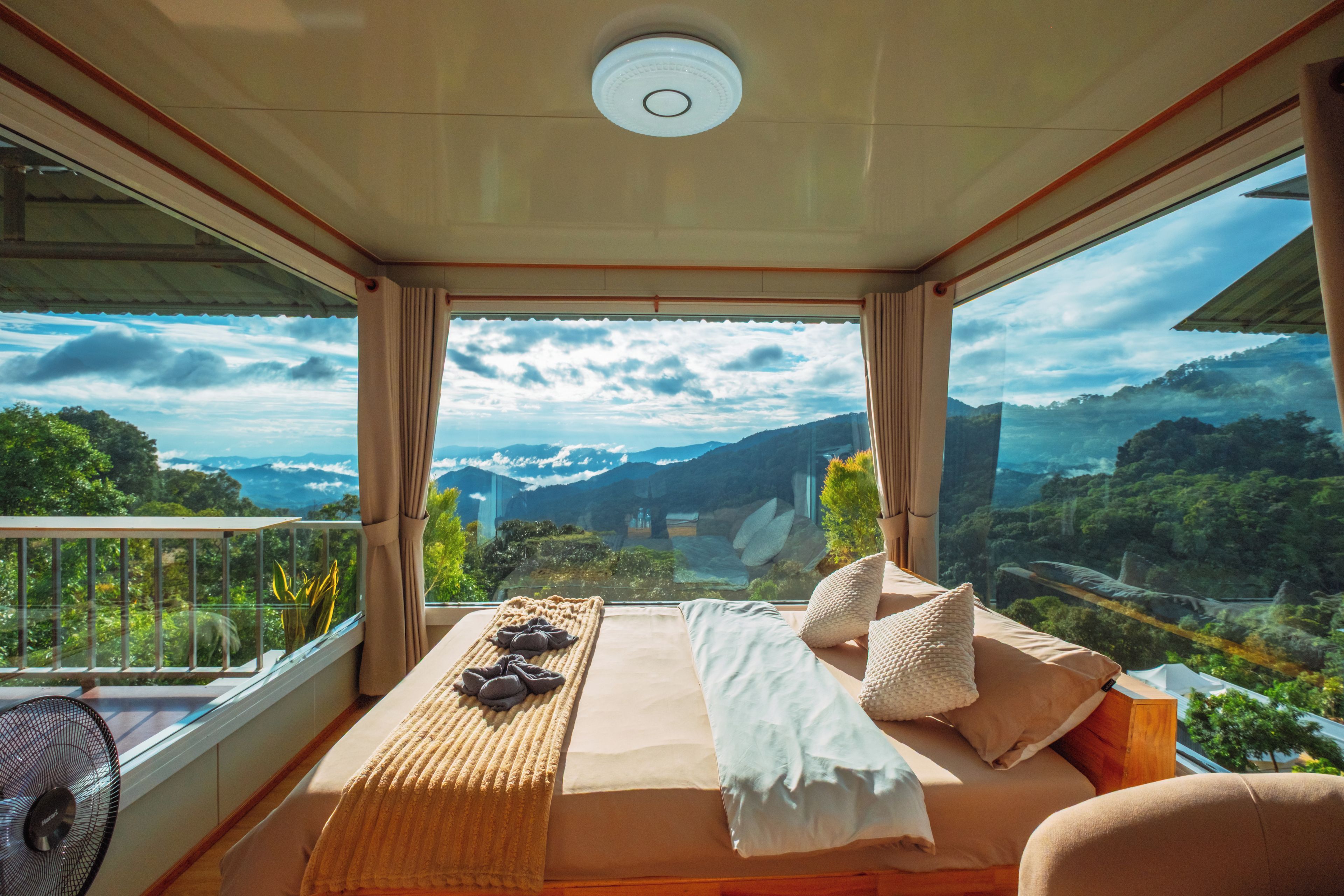 A balcony with a bed, a fan, and a view of the mountains.