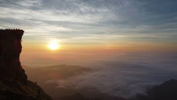 A sunrise over a mountainous landscape with a cliff on the left and clouds below.