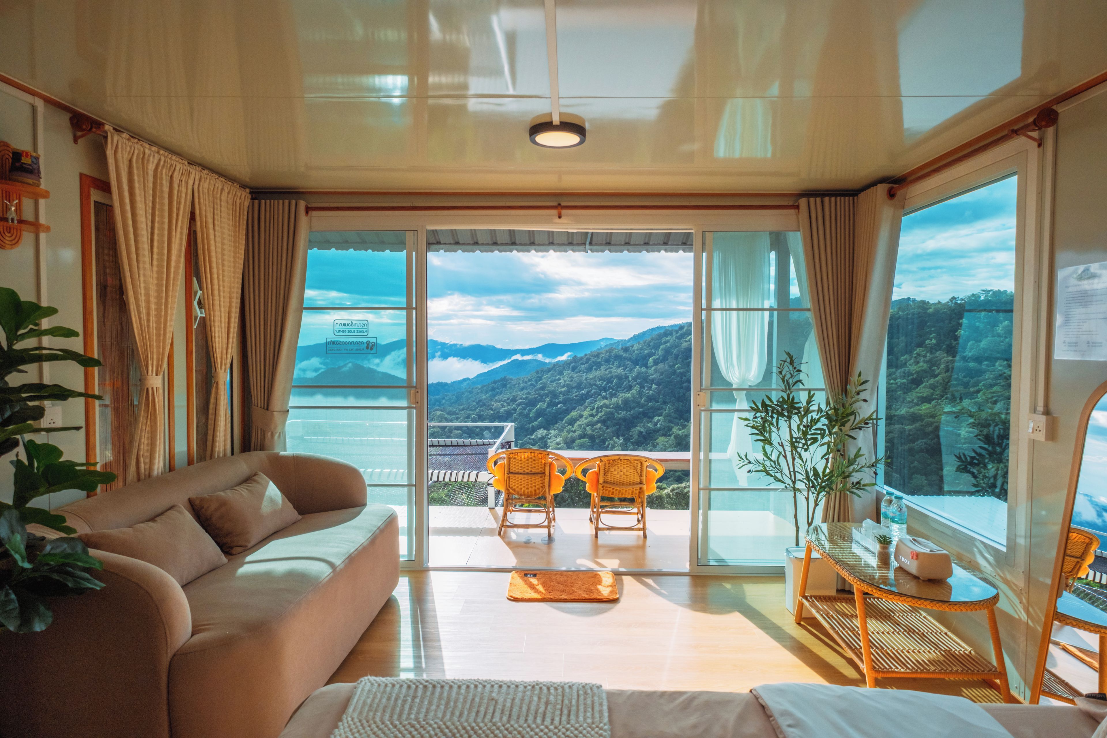 A room with a sofa, two chairs, a small table, and a view of mountains through large windows.