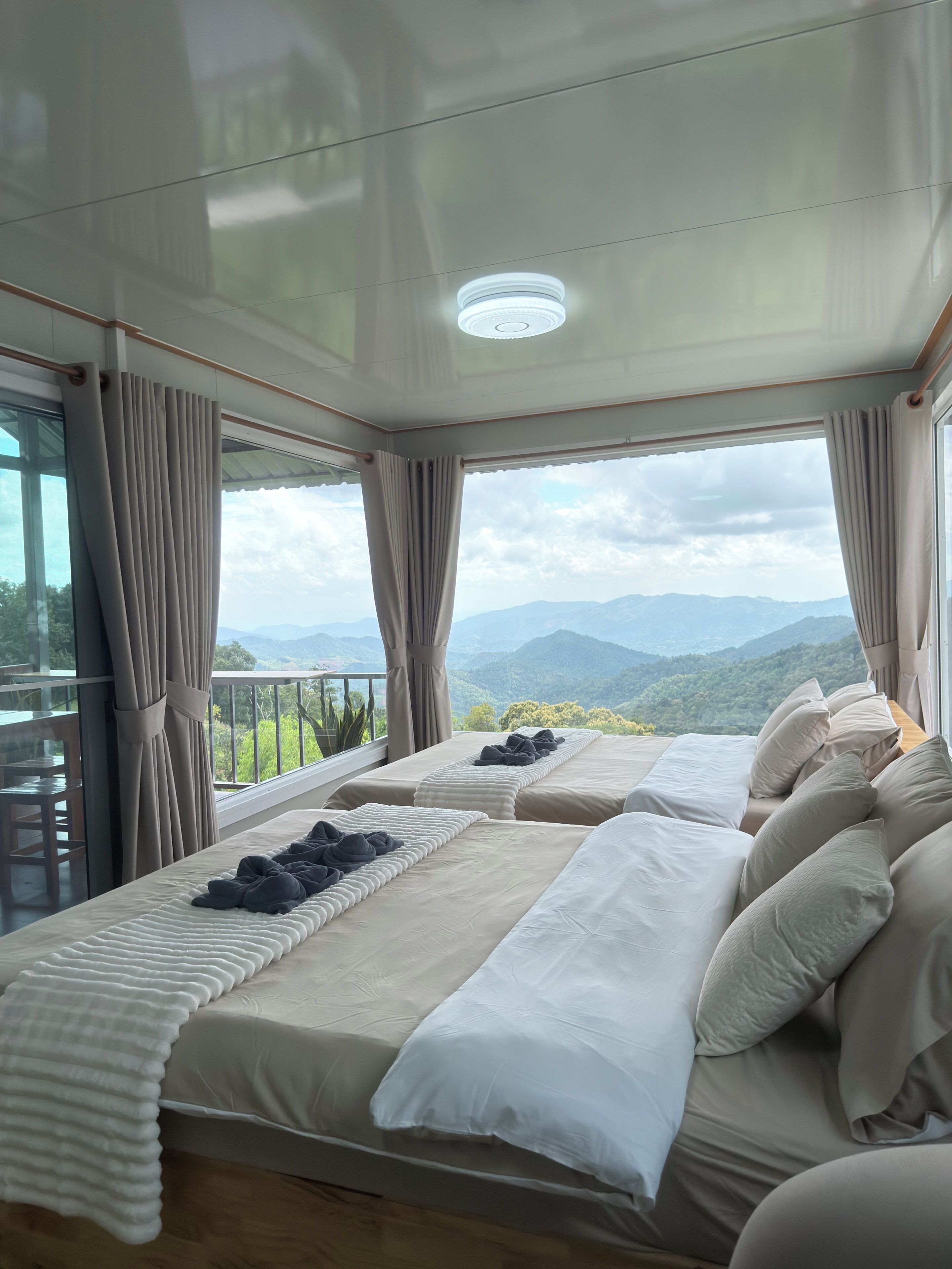 A bedroom with two beds, a balcony, and a view of mountains.
