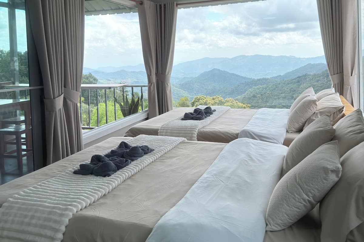 A bedroom with two beds, a balcony, and a view of mountains.
