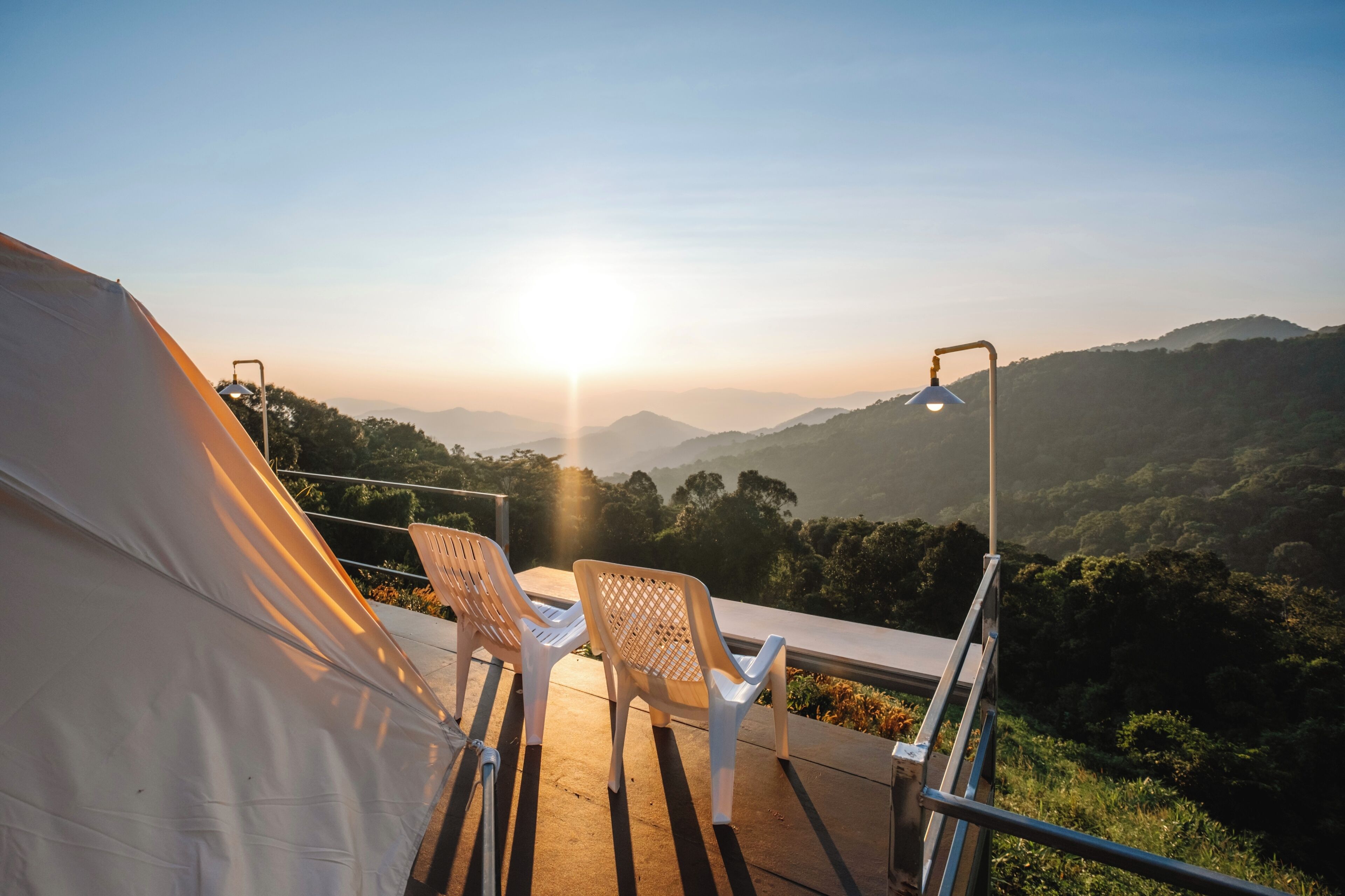 A tent with two chairs and a table, overlooking a mountainous landscape during sunset.