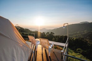 Una carpa con dos sillas y una mesa, con vistas a un paisaje montañoso durante el atardecer.