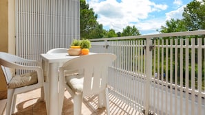 Een balkon met een witte tafel en stoelen, een kleine potplant en een mand met sinaasappels.