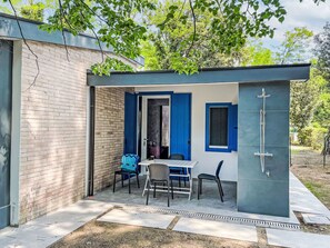 Un espacio exterior pequeño y cerrado con una mesa, sillas, una puerta azul y una zona de ducha.