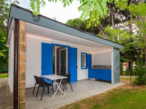 Una cocina moderna al aire libre con comedor, que incluye una mesa y sillas, y una parrilla de barbacoa integrada.