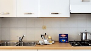 Eine Küche mit weißen Schränken, einer Edelstahl-Spüle, einem Herd und einer Packung Barilla Pasta.
