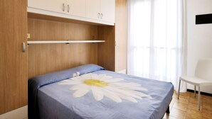Une chambre à coucher avec un lit, une armoire en bois, une chaise et une fenêtre avec des rideaux.