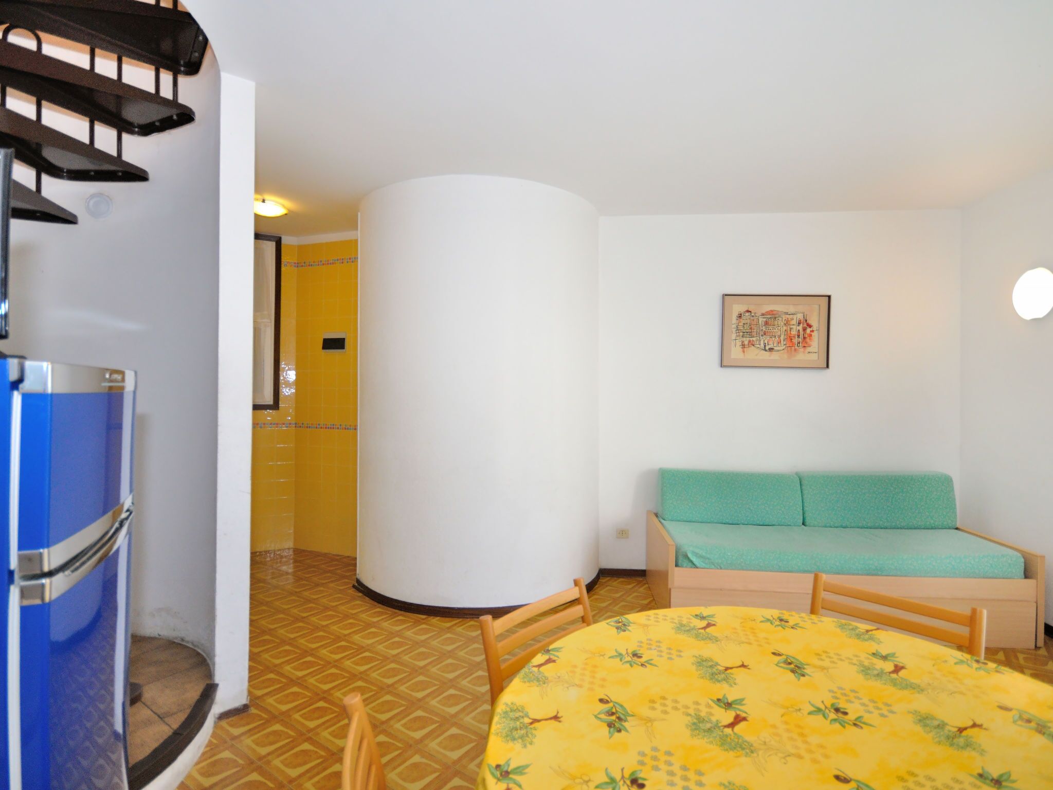 Una habitación pequeña con cama, una mesita, una silla y un refrigerador.