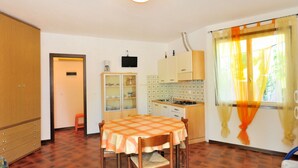 A compact kitchen with a dining table, wooden cabinets, and a window with curtains. - Villaggio Tivoli by Interhome (Bibione)