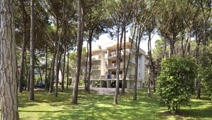 A multi-story building with balconies, surrounded by trees and grass. - Boschetto by Interhome (Bibione)