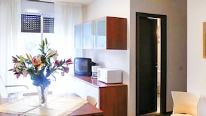 A small, well-lit kitchen with a microwave, toaster, and cabinets. There is a dining table with chairs and a vase of flowers. - Apartment Erica by Interhome (Bibione)