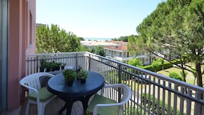 A balcony with a round table and two chairs, overlooking a residential area with trees and a distant view of buildings. - Apartment Erica by Interhome (Bibione)