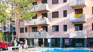 A swimming pool area with a building in the background. - Apartment Erica by Interhome (Bibione)