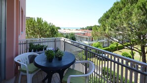 A balcony with a round table and two chairs, overlooking a residential area with trees and a distant view of buildings. - Apartment Erica by Interhome (Bibione)