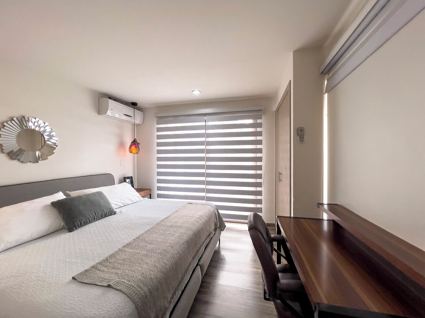 A bedroom with a bed, bedside table, lamp, and a window with blinds.