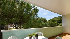 Un balcón con una mesa redonda, dos sillas blancas y tres macetas.