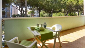 Een balkon met een tafel gedekt voor twee personen, met uitzicht op een gebied met bomen en gebouwen op de achtergrond.