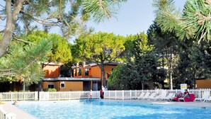 A swimming pool with a white fence, surrounded by trees and a building with a yellow facade. - Villaggio Splendido by Interhome (Bibione)