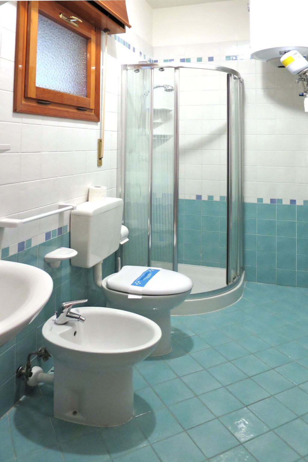 A bathroom with a toilet, bidet, and sink, a shower with a glass door, and tiled walls.