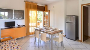 A compact kitchen with a dining table, chairs, a refrigerator, a TV, and a window with curtains. - Villaggio Splendido by Interhome (Bibione)