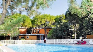 Une piscine entourée d’une clôture blanche, bordée d’arbres et située à proximité d’un bâtiment à la façade jaune.